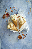 Almond and honey ice cream,prepared in three crispy ice cream cones,arranged on a white plate,decorated with almonds and honey on a blue background