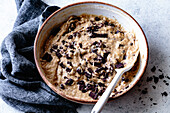 A bowl of cookie dough with chunks of dark chocolate, accompanied by a textured gray kitchen towel.