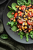 Salat mit Kichererbsen,schwarzem Reis,Tomaten,Mandeln und Grünzeug auf einem schwarzen Teller. Schwarzer Hintergrund