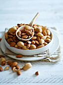 A white bowl with peeled and unpeeled almonds on a white wooden background