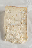 A piece of Italian cheese called Gorgonzola lying on the paper in which it is wrapped. Front view