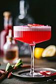 A close shot of a sophisticated alcoholic beverage, featuring a textured stemmed coupe cocktail glass with colorful red liquor with a foamy top