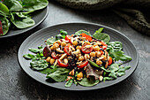 Salat mit Kichererbsen,schwarzem Reis,Tomaten,Mandeln und Grünzeug auf einem schwarzen Teller. Schwarzer Hintergrund
