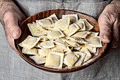 The skilful hands of a chef holding a wooden plate of raw ravioli, fresh and expertly shaped, ready for cooking