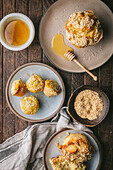 A flat lay image of a rustic wooden table with a light grey cloth, honey in a white bowl, a bowl of sesame seeds, and sesame seed muffins on beautiful natural colored plates.There is a wooden honey dipper with the large muffin. The muffins are all topped with sesame seeds.