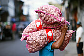 Daily worker at traditional food market, man carrying heavy bags with garlic on his head, Surabaya, Java, Indonesia, South East Asia, Asia