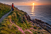 Walker looking out to sea from the Anglesey Coast Path at sunset in spring, near Cemaes, Anglesey, North Wales, United Kingdom, Europe