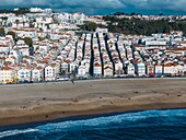 The lively beach, revealing rows of charming houses with red roofs and people enjoying the sandy shore under a clear sky, Nazare, Oeste, Estremadura, Portugal, Europe