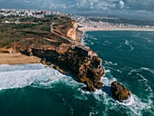 Luftaufnahme von Touristen am historischen Leuchtturm Sao Miguel Arcanjo mit Blick auf die atemberaubende Küstenlinie von Nazare mit riesigen Wellen,die eine spektakuläre Aussicht genießen,Nazare,Oeste,Estremadura,Portugal,Europa