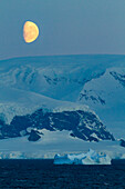 Blick auf den fast vollen Mond,der über schneebedeckten Bergen auf der Antarktischen Halbinsel aufgeht,Antarktis,Polarregionen