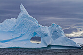 Ungewöhnliche Fensterformation in einem Eisberg mit Booth Island im Hintergrund auf der Westseite der Antarktischen Halbinsel,Antarktis,Polarregionen