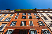 Colorful Roman houses with balconies stretch along Frattina Street beneath a bright blue sky.