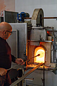 The glassblower reinserts the piece into the furnace in a glassblowing demonstration in Venice, Italy.