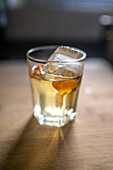 A close up of a refreshing whiskey cocktail garnished with orange peel and ice, captured in the vibrant city of Seville, Spain. Perfect for leisure and celebration settings.