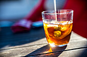 A close up of a refreshing glass of vermouth with ice and olive garnish. The sunlight enhances the vibrant colors, creating an inviting beverage scene.