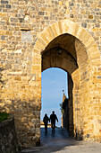 A couple walks through the Porta Roma gate into the medieval walled town of Monteriggioni, Sienna, Tuscany, Italy.