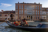 Tourists in a gondola in front of the Palazzo Genovese, built in 1892 on the Grand Canal in Venice, Italy.