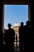 Tourists pass through an archway, revealing Saint Peter's Basilica under a clear sky in Vatican City, showcasing its grand architecture.