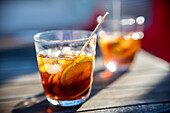 A close up of two glasses filled with refreshing vermouth cocktails on a sunlit patio table, highlighting the vibrant colors and inviting ambiance.