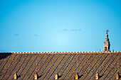 Ein klarer blauer Himmel über einem traditionellen Dach in Sevilla,Spanien,mit dem ikonischen Turm La Giralda im Hintergrund,der den historischen Charme der Stadt einfängt.