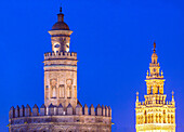 Eine nächtliche Ansicht von Sevilla mit dem Torre del Oro und La Giralda unter einem strahlend blauen Himmel. Das Foto fängt die historische Schönheit und architektonische Pracht dieser Wahrzeichen ein.