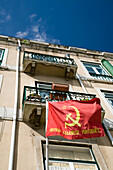 The office of the Portuguese Communist Party displays a red flag in Alfama, featuring traditional architecture against a clear blue sky.