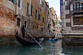 A gondola carrying tourists navigating a canal in Venice, Italy.