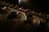 Aerial night view of an abundant Ebro River passing under the Stone Bridge after the Dana, Zaragoza, Spain