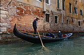 A gondola carrying tourists navigating a canal in Venice, Italy.