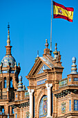 Close up of the intricate architectural details of Plaza de España in Seville, Spain, featuring traditional Spanish design elements and a vibrant flag against a clear blue sky.