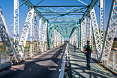 Sevilla,Spanien,17. September 2024,Urbane Szene mit Menschen auf Elektrorollern auf der 1930 erbauten historischen Eisenbrücke San Juan über den Fluss Guadalquivir in Sevilla,Spanien. Das Brückenbauwerk dominiert die Landschaft.