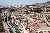 The view captures the vibrant urban and coastal landscape of Malaga, showcasing buildings and greenery from above.