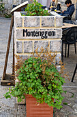 A metal sign on a stone planter box in the medieval walled town of Monteriggioni, Sienna Province, Italy.