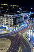 The vibrant nightlife of Restauradores Square in Lisbon showcases light trails from cars navigating the urban streets at night.