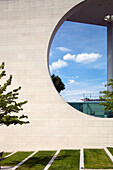 Das moderne Gebäude des Bundeskanzleramts in Berlin zeichnet sich durch ein auffälliges rundes Fenster und üppiges Grün im Vordergrund aus.