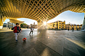 Seville, Spain, Jan 28 2021, Young children joyfully plays with a ball under the iconic Las Setas structure in Sevilla, Spain. The architectural beauty and sunlit surroundings create a vibrant urban scene.