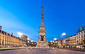 Restauradores Square in Lisbon illuminates the night with vibrant light trails from passing traffic, featuring the grand monument.