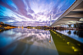 Beautiful dusk scene capturing the illuminated Alamillo Bridge over Rio Guadalquivir in Sevilla, Spain. The reflection on the water adds tranquility to the vibrant cityscape.