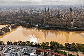 Aerial view of an abundant passing by El Pilar Basilica Cathedral after the Dana, Zaragoza, Spain