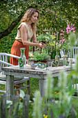 Woman sets table with herbs, vases with fennel, oregano, mint