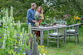 Couple in front of a laid table, vases with herbs, fennel, oregano, mint in vases