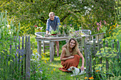 Couple with dog in front of a laid table, vases with herbs, fennel, oregano, mint