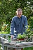 Man decorates garden table, bouquet of flowers with spice fennel, Indian nettle, oregano, mint in the garden