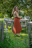 Woman holding a flower pot with fennel, oregano and mint in front of a garden table