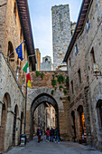 Touristen auf der Via San Matteo in der Nähe des Kanzleitors in der mittelalterlichen Stadt San Gimignano, Italien. Dahinter befinden sich der Torre Rognosa und der Torre Salvucci.