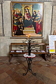 Madonna on the Throne by Ridolfo di Ghirlandaio in the nave of the Church of Sant'Agostino in San Gimignano, Italy. In front are votive candles on a metal tree sculpture.