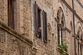 A man looks out his window from a building on the Via San Giovanni in the walled town of San Gimignano, Italy.