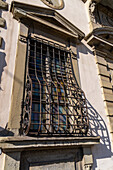 An ornate cast iron window grate on a building with Renaissance architecture in Florence, Italy.