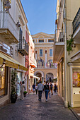 Tourists walk past high-end luxury shops on the Via Vittorio Emmanuele in Capri, Italy. Behind is the Grand Hotel Quisisana.