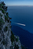 A tour boat motors in the Bay of Naples in the Tyrrhenian Sea below the cliffs of the island of Capri, Italy.